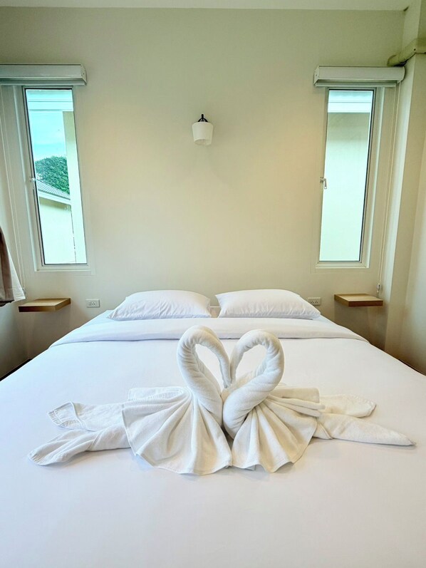 Una habitación de hotel con una cama, dos mesitas de noche, una lámpara de pared y dos ventanas.