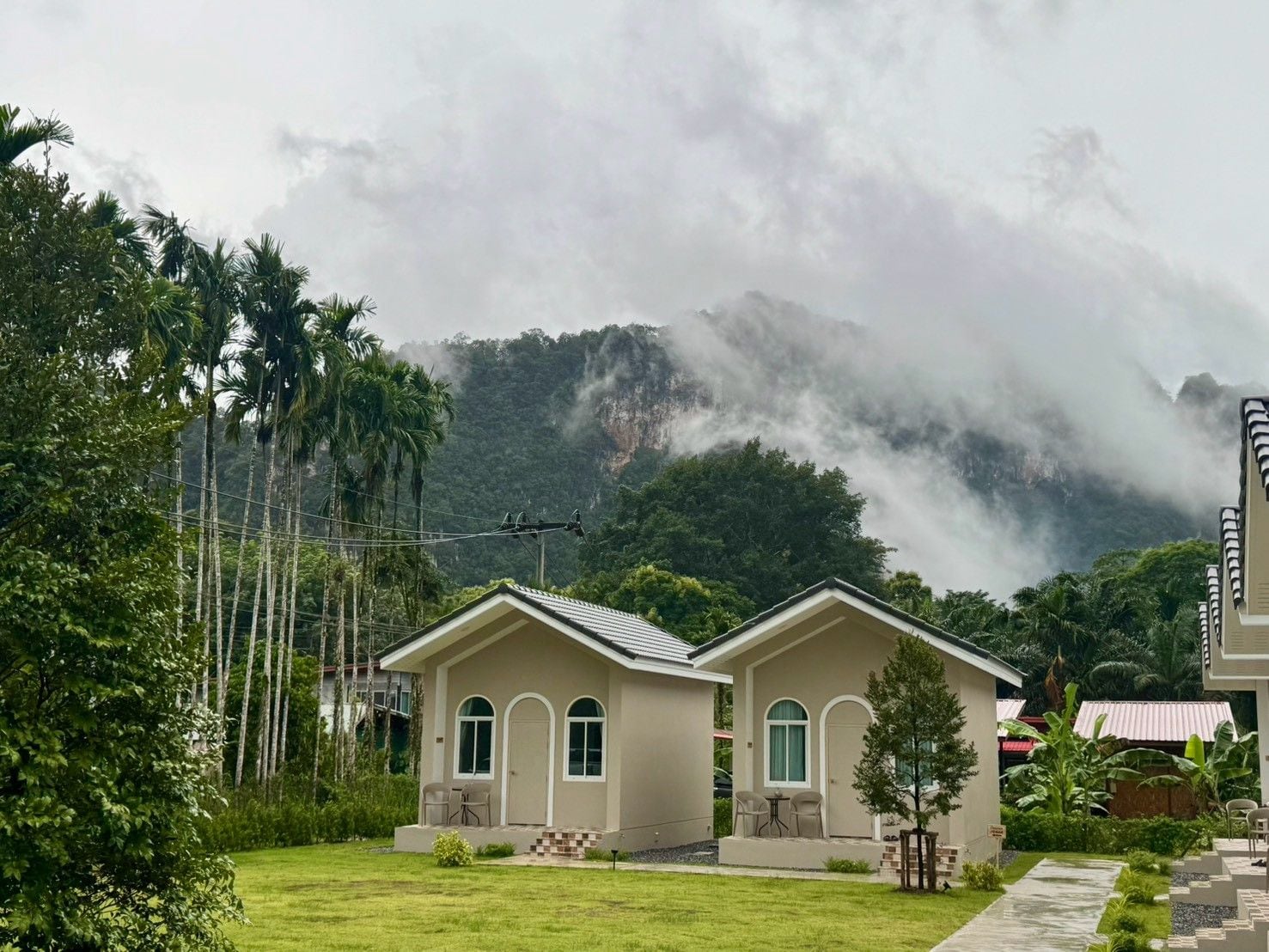 A two-story house with a flat roof, a front porch with chairs, and a view of a mountainous landscape.