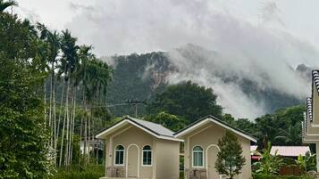 A two-story house with a flat roof, a front porch with chairs, and a view of a mountainous landscape.