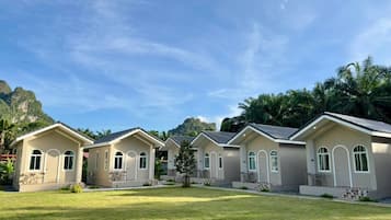 A row of modern, single-story buildings with large windows and a flat roof, surrounded by a well-maintained lawn and palm trees, with a mountainous backdrop.