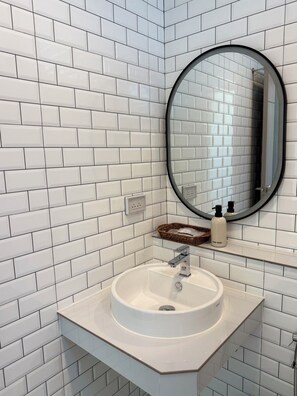 A bathroom with white subway tiles, a round mirror, a white sink, and a small wicker basket.