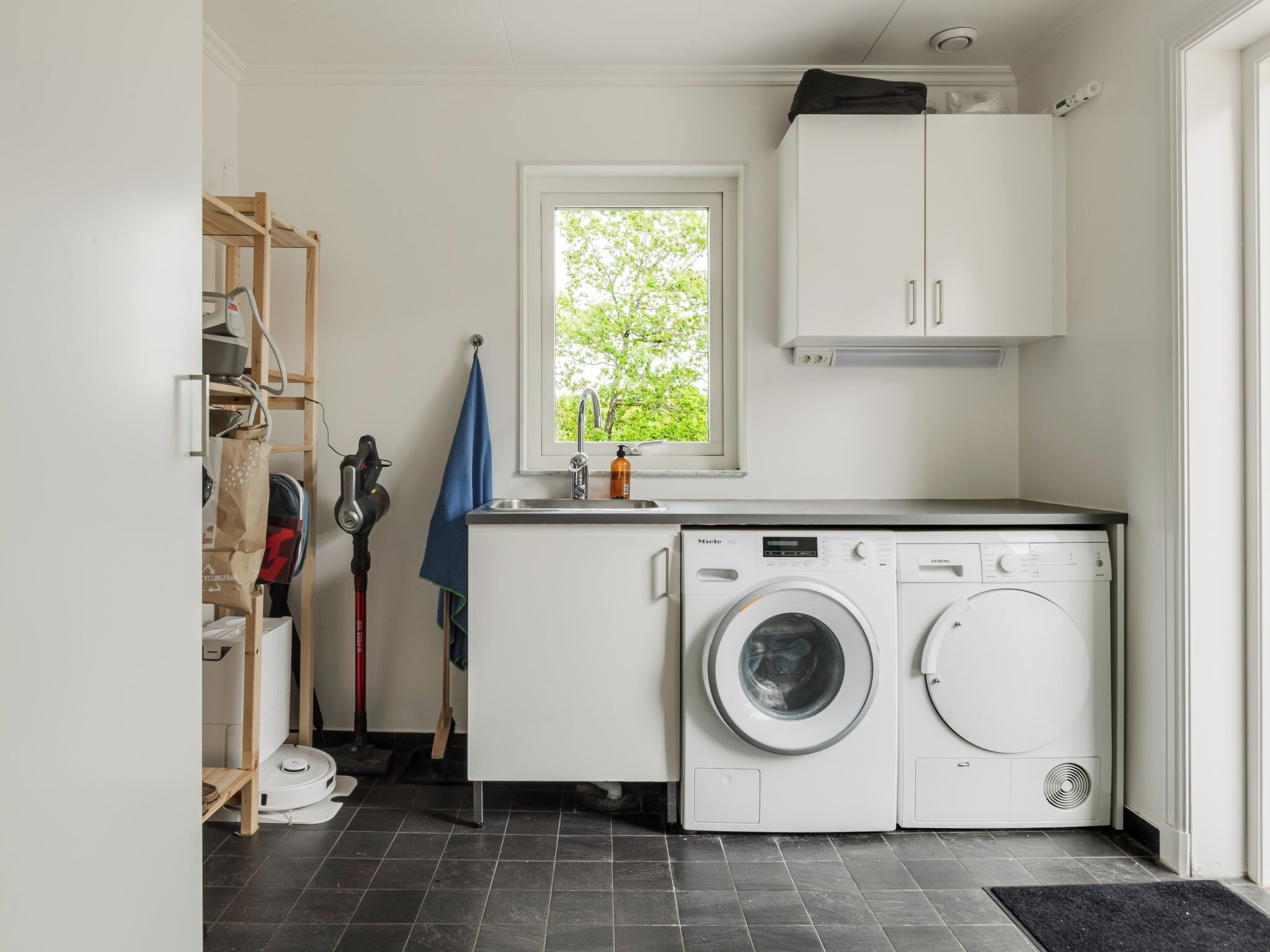 A compact laundry room with a washing machine, a dryer, and a window with a view of trees.