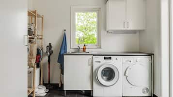 A compact laundry room with a washing machine, a dryer, and a window with a view of trees.