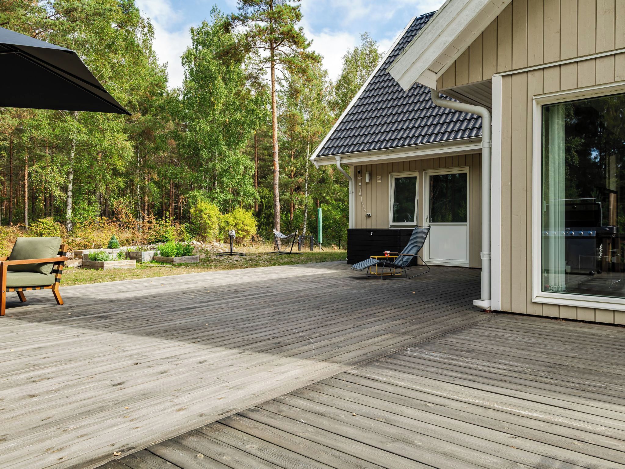 En træterrasse med udendørs møbler, et overdækket siddeområde og et hus med store vinduer.