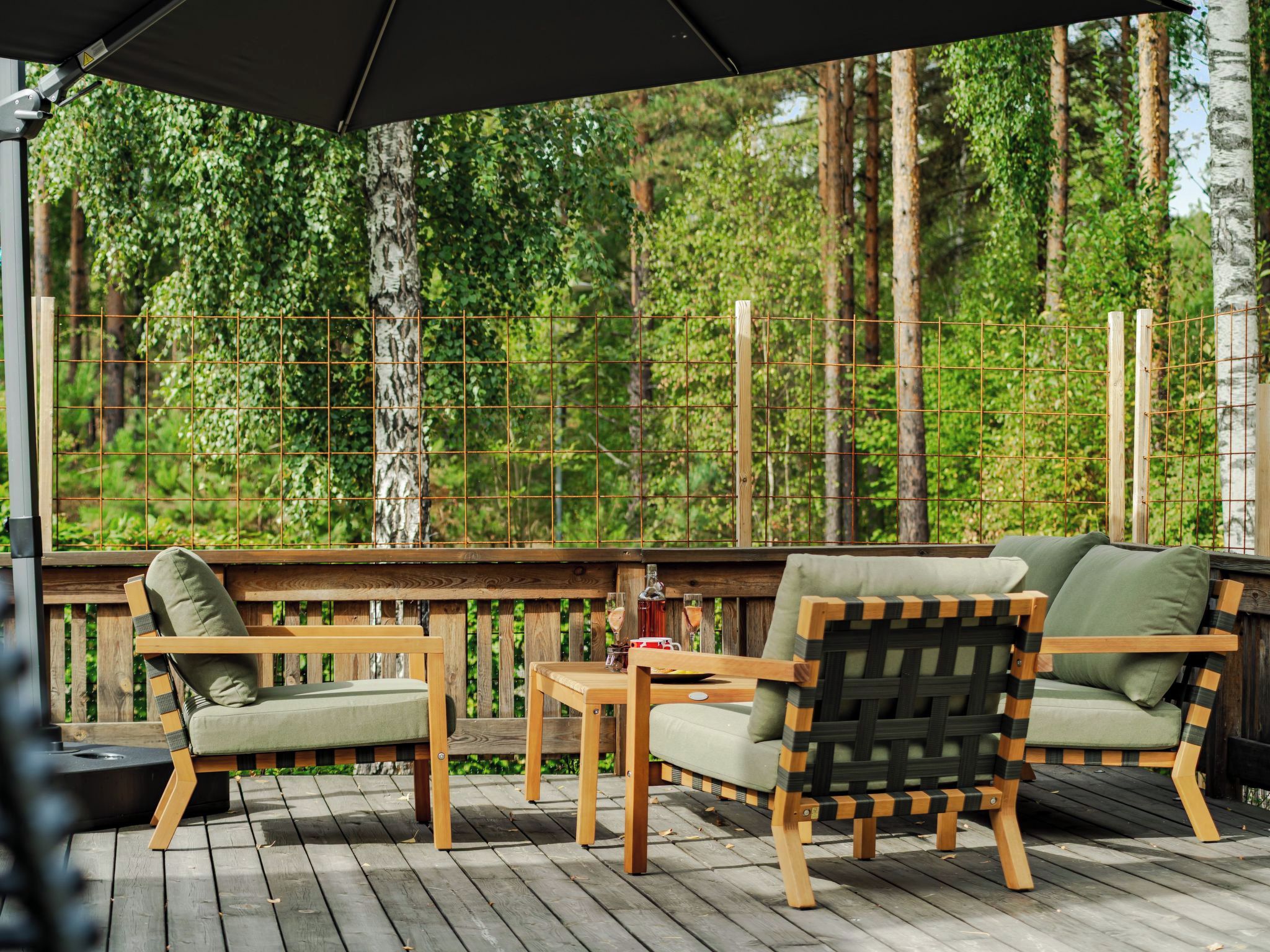 A wooden deck with outdoor furniture, including chairs and a table, overlooking a forested area.
