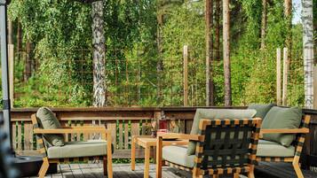 A wooden deck with outdoor furniture, including chairs and a table, overlooking a forested area.