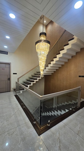 A modern staircase with a glass railing, a chandelier, and a polished floor. - Hotel Mahakal Palace (Ujjain)
