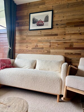A living room with a wooden wall, a framed picture, a sofa, and a chair. - Le Dahut Blanc, a charming retreat at the foot of the slopes (Morillon)