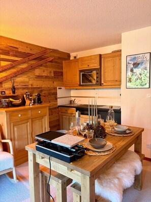 A cozy kitchen with wooden cabinets, a built-in microwave, and a dining table set for a meal. - Le Dahut Blanc, a charming retreat at the foot of the slopes (Morillon)