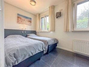 Een slaapkamer met twee bedden, een raam met gordijnen, een wandlamp en een radiator.