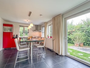 Een moderne keuken met een rode apparatuur, een eethoek met barstoelen en grote ramen met gordijnen.