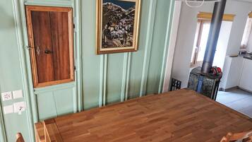 A dining area with a wooden table and chairs, a framed painting on the wall, and a kitchen area with a stove.