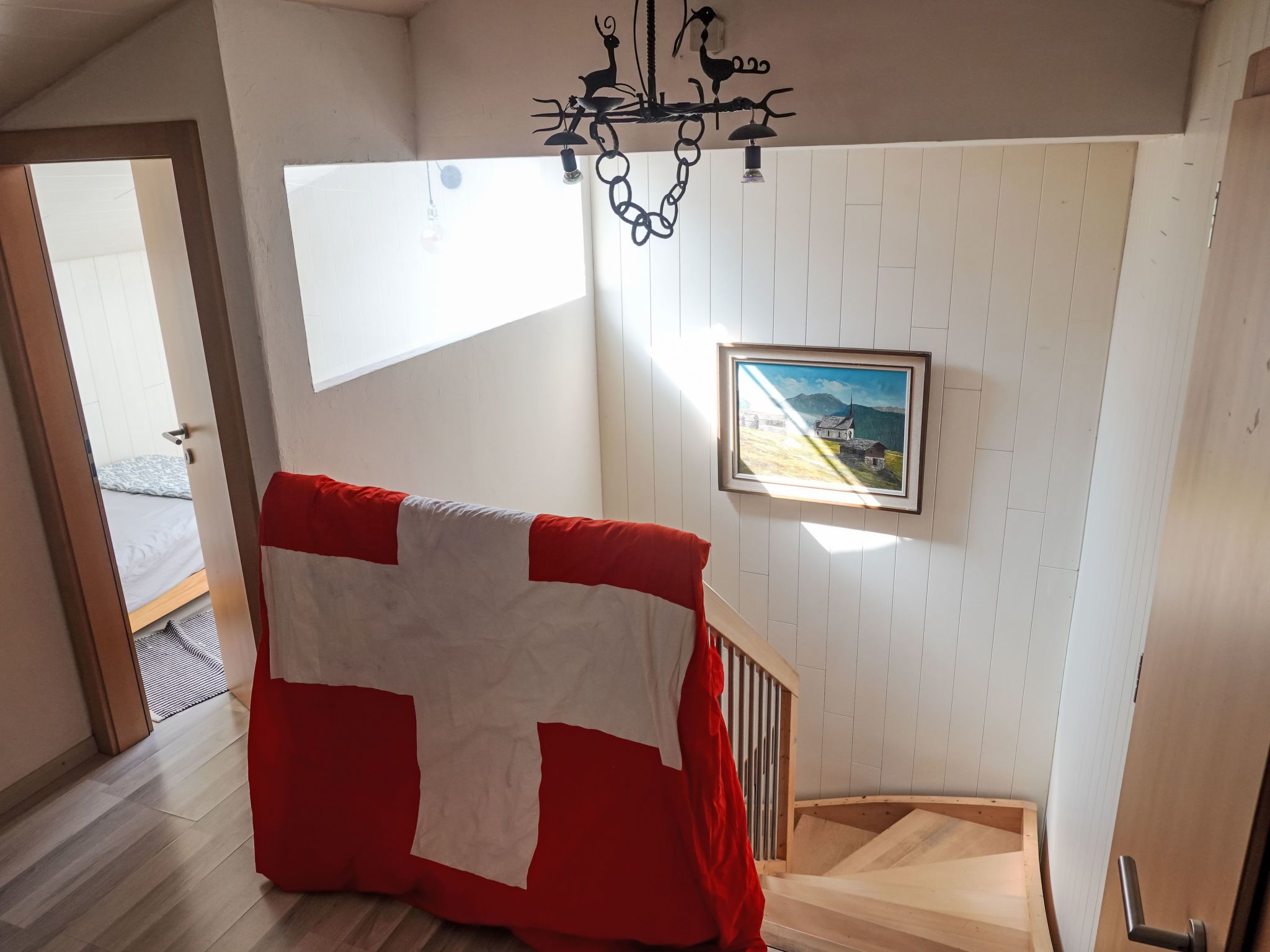 A staircase with a red and white blanket draped over it, a framed picture on the wall, and a chandelier.