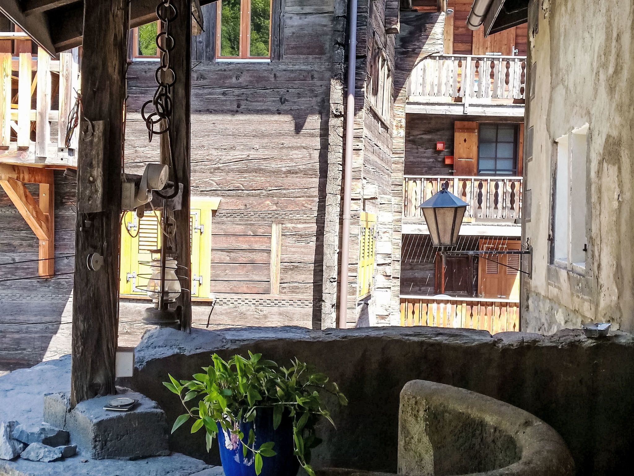 A rustic wooden building with a balcony, a stone wall, and a potted plant.