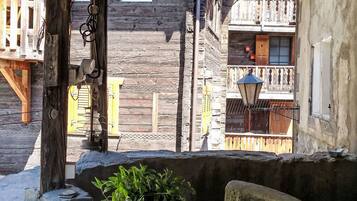 A rustic wooden building with a balcony, a stone wall, and a potted plant.
