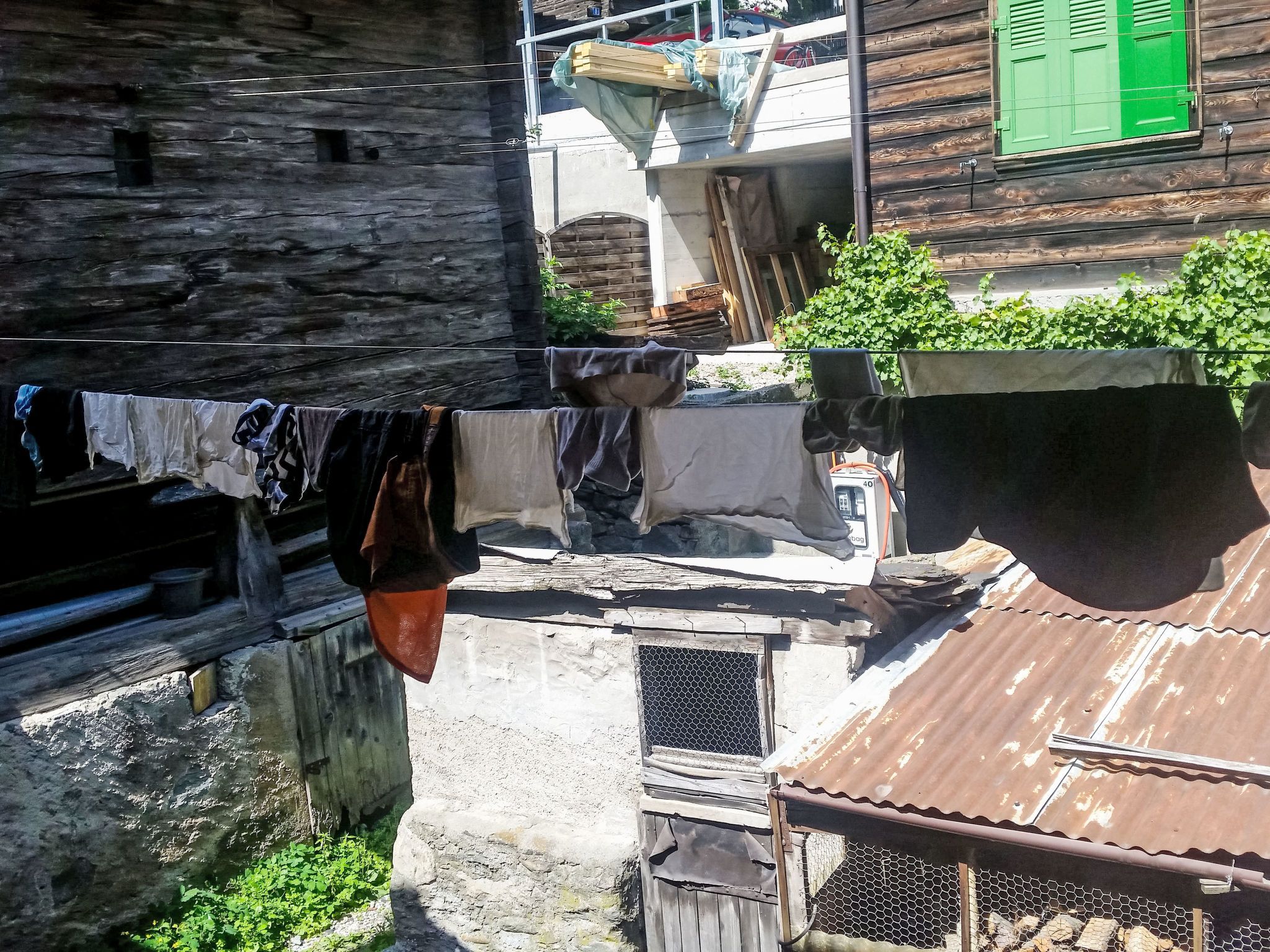 Un carrer estret amb edificis de fusta, una corda de roba amb diferents peces i una reixa metàl·lica.