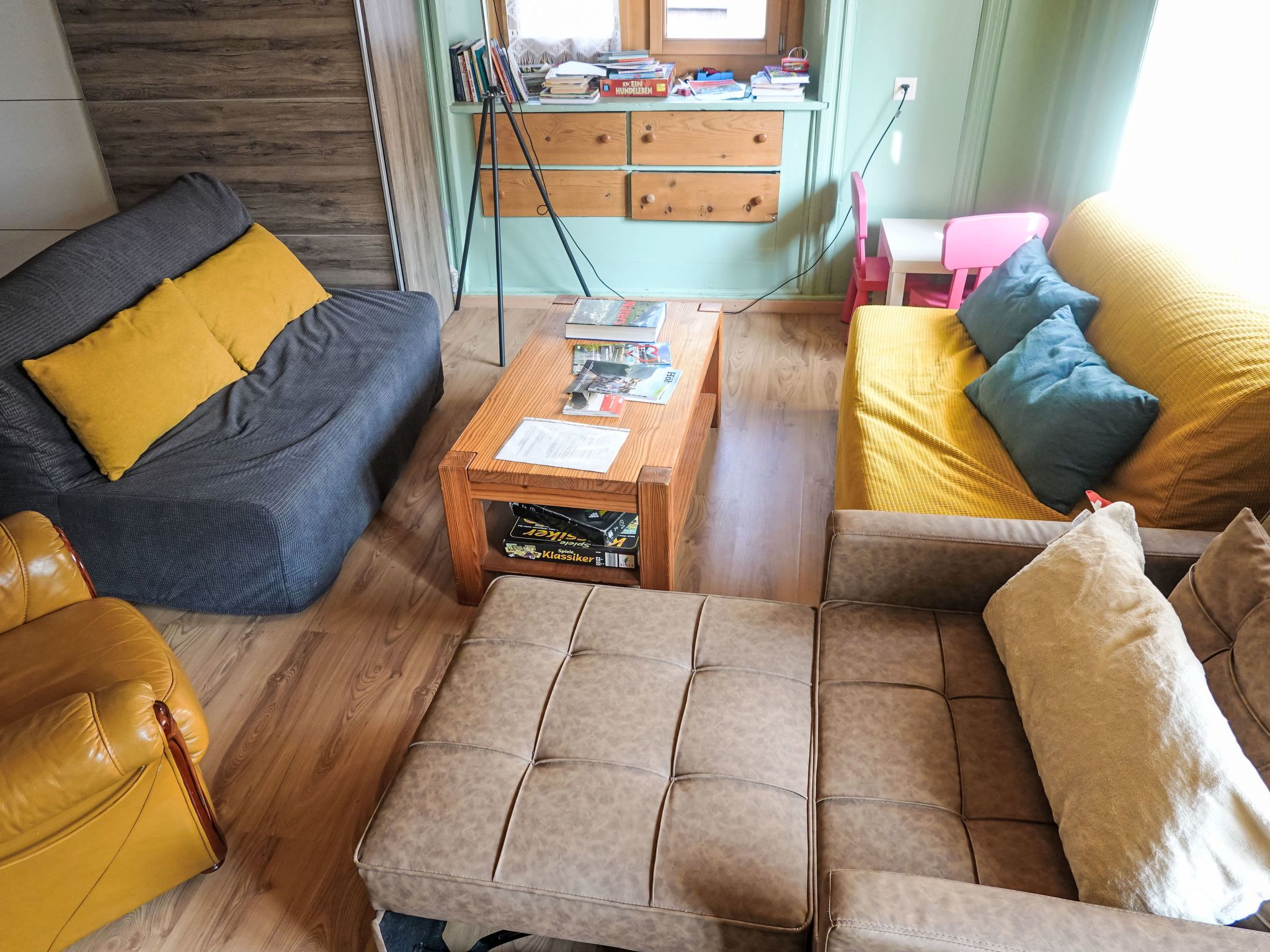 A living room with a sofa, armchair, ottoman, and a coffee table with magazines.