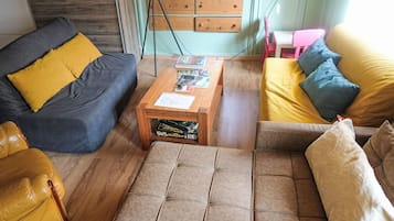 A living room with a sofa, armchair, ottoman, and a coffee table with magazines.