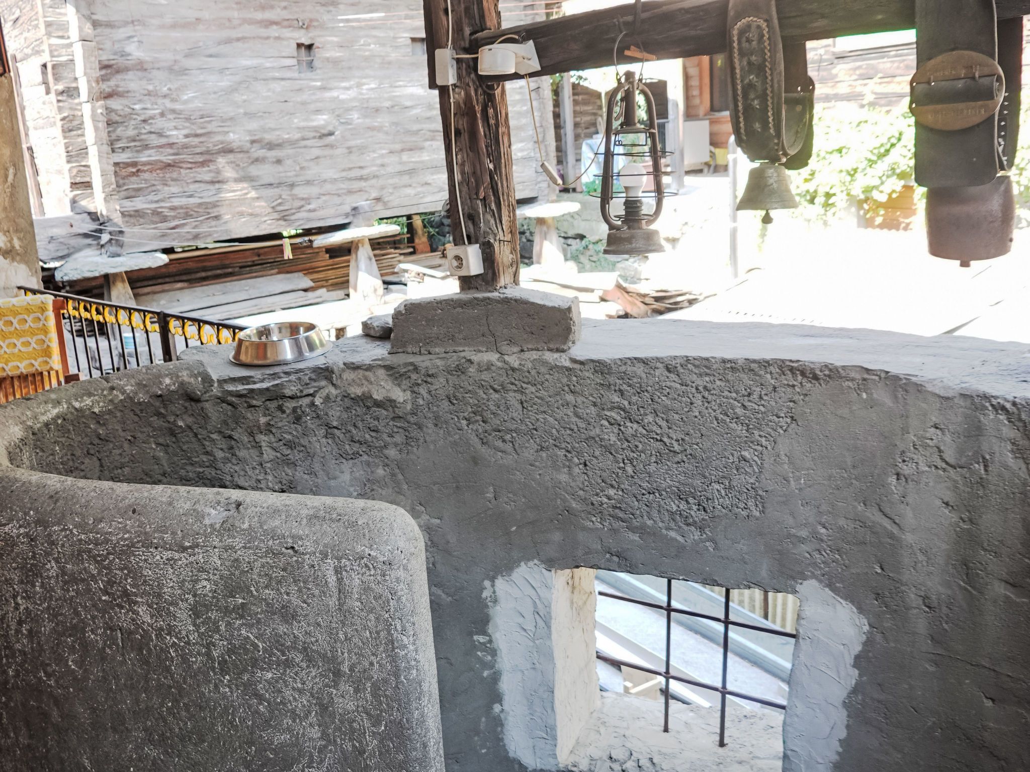 A rustic interior with a concrete structure, a metal railing, and a metal bowl on a rock.