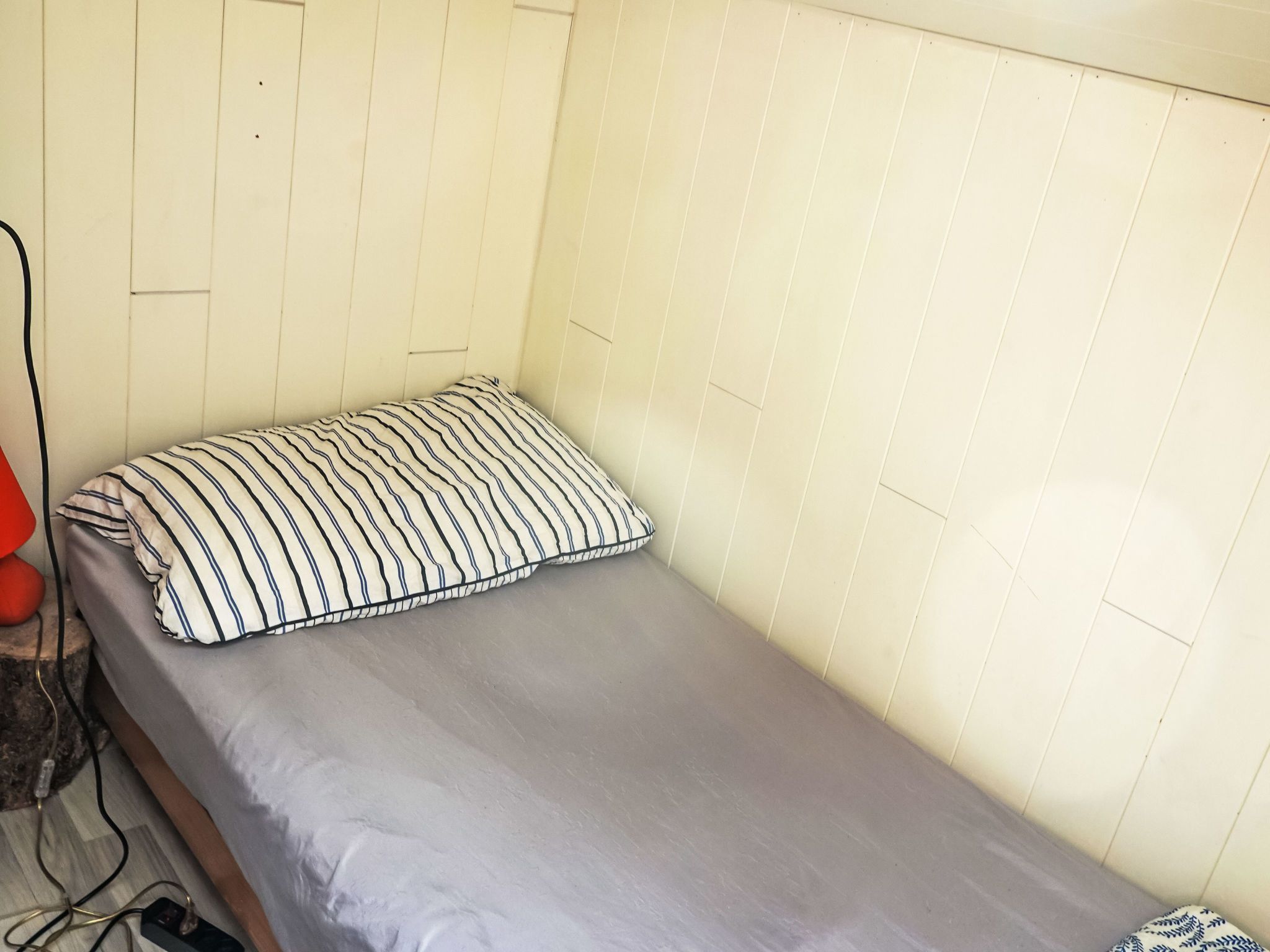 Habitació petita amb un llit individual, un matalàs gris i un coixí ratllat.