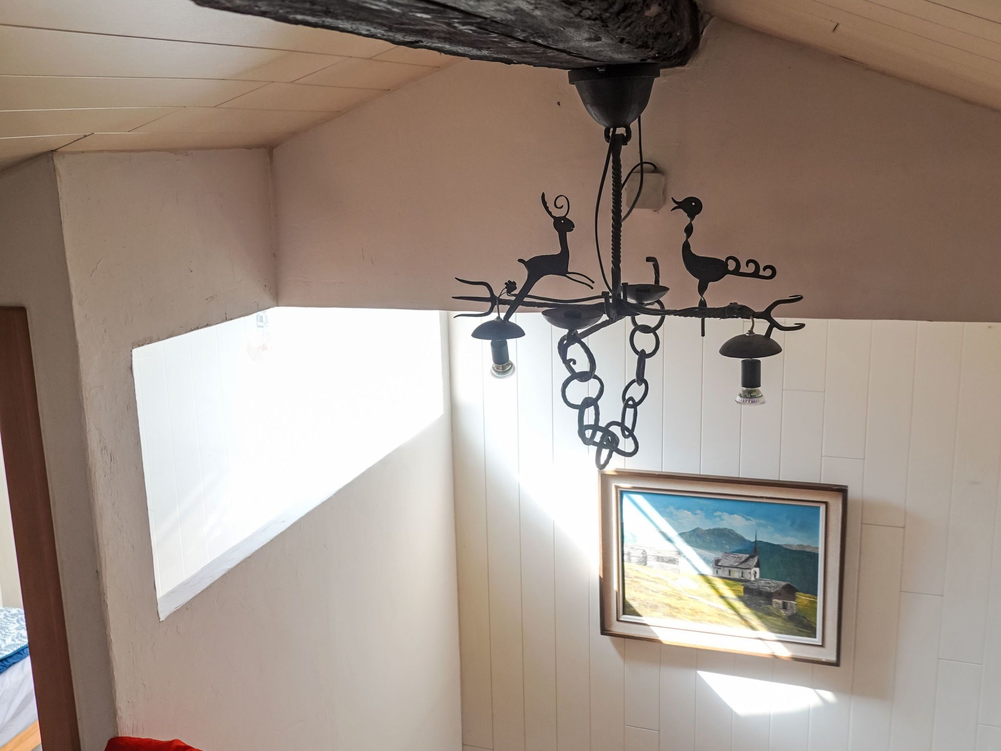 A room with a white wall, a framed painting, and a black chandelier with animal silhouettes.