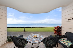 A patio with a view of the ocean, a round table with chairs, and a decorative plant. - Ground-Floor Oceanfront 1BD with AC & Island Views -Kahana Reef 120 (Lahaina)