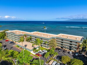 A multi-story hotel with a parking lot and a view of the ocean. - Ground-Floor Oceanfront 1BD with AC & Island Views -Kahana Reef 120 (Lahaina)