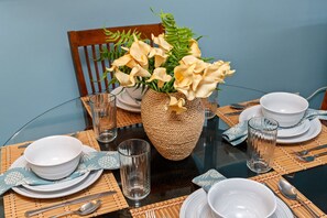 A round dining table with a woven centerpiece, white plates, and clear glassware. - Ground-Floor Oceanfront 1BD with AC & Island Views -Kahana Reef 120 (Lahaina)