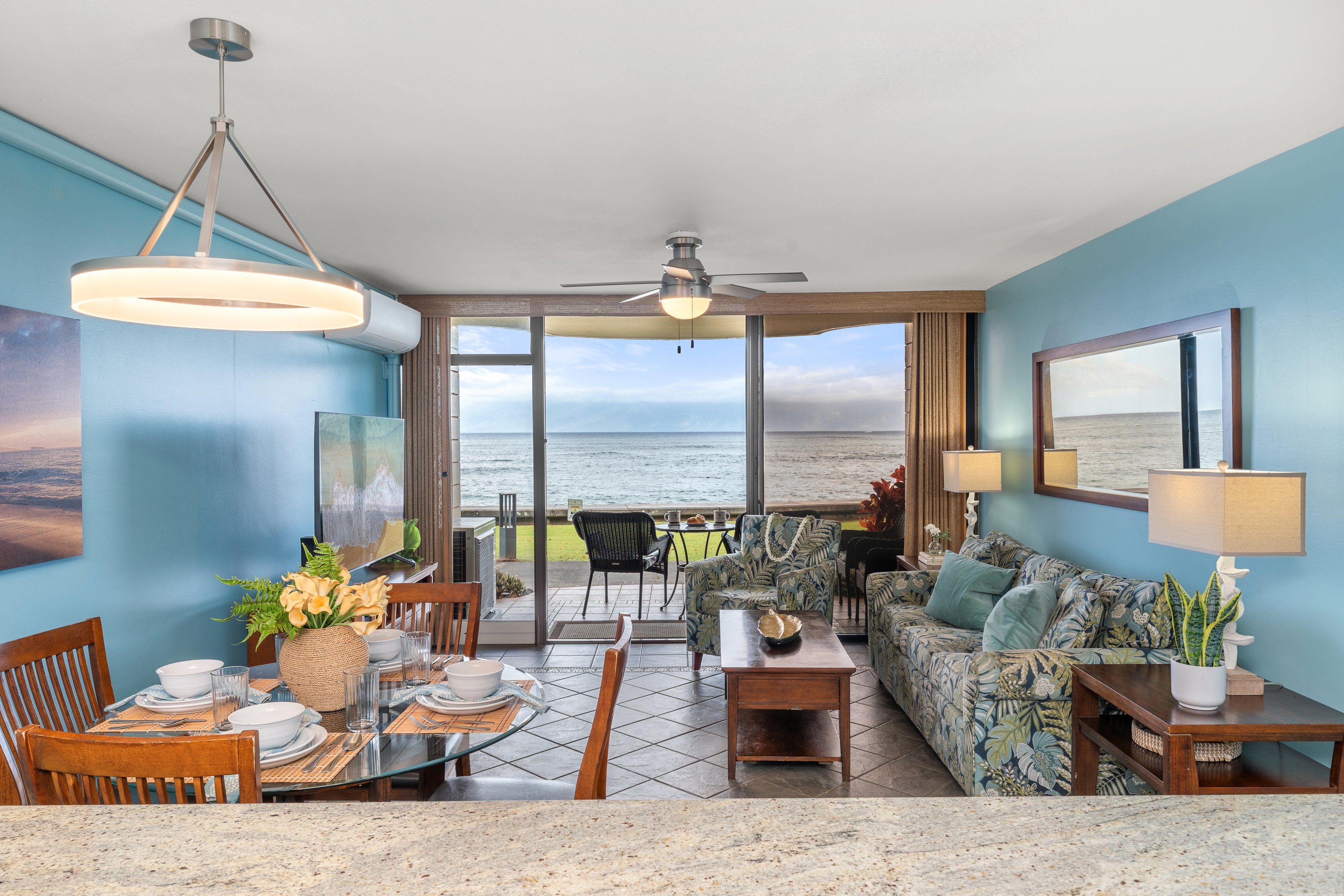 A room with a view of the ocean, featuring a dining area, a sofa, and a ceiling fan.