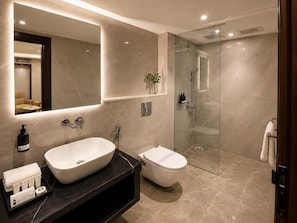 A modern bathroom with a large mirror, a freestanding sink, a toilet, and a glass-enclosed shower area. - Hotel Midtown (Jamshedpur)