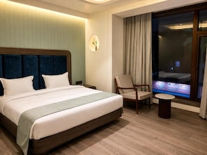 A hotel room with a large bed, a chair, a small table, and a TV screen. - Hotel Midtown (Jamshedpur)