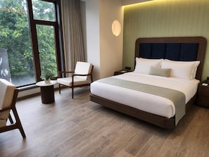 A hotel room with a large bed, a chair, a small table, and a window with a view of trees. - Hotel Midtown (Jamshedpur)