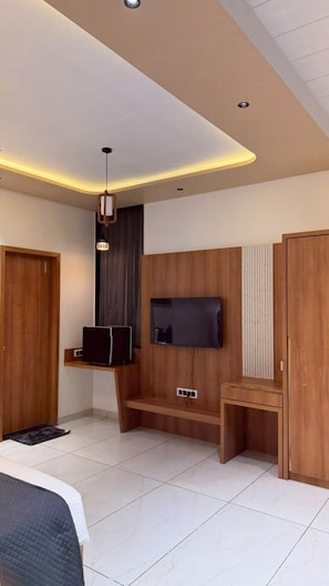 A modern bedroom with a bed, a TV mounted on the wall, and a wooden bench. - The Premier Girtara Resort (Talala)