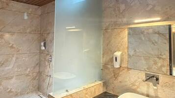 A modern bathroom with a glass shower enclosure, a marble-tiled floor, and a wooden vanity with a sink.