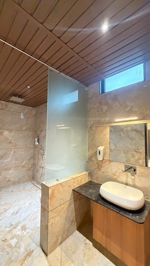 A modern bathroom with a glass shower enclosure, a marble-tiled floor, and a wooden vanity with a sink.