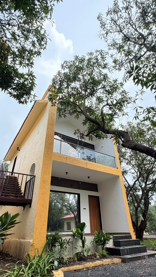 A two-story building with a balcony on the upper floor, surrounded by greenery.