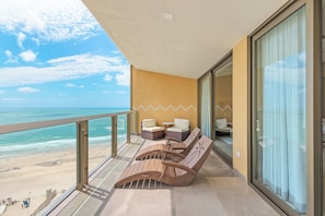 Un balcon avec vue sur la plage, une table avec des chaises et un canapé.