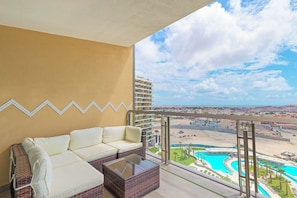 A balcony with a white sofa and a glass coffee table, overlooking a pool and a cityscape. - Sonoran Star 1106-02 – Seaside Ocean View Paradise (Puerto Peñasco)