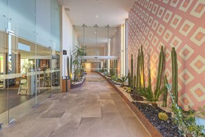 Un couloir bordé de vitrines, un mur orné de motifs et une variété de plantes, dont des cactus.