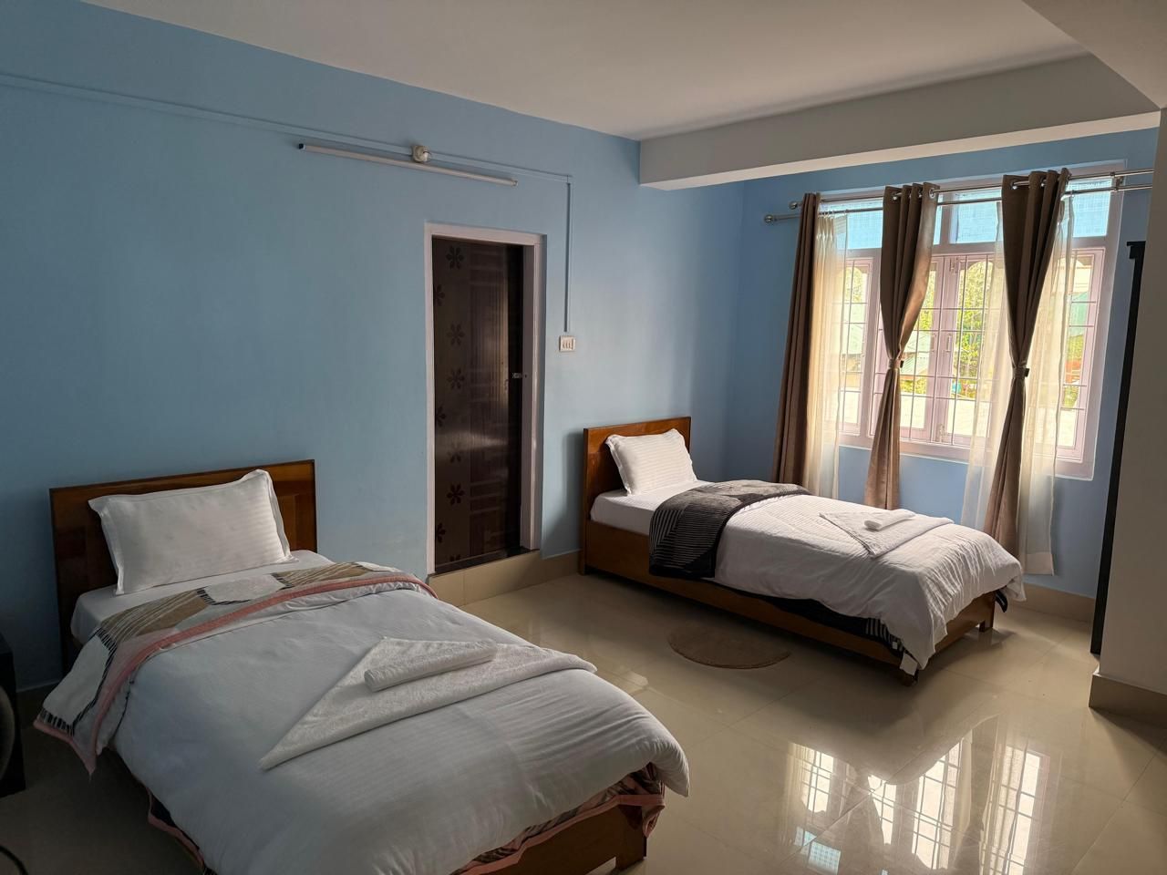 Una habitación con dos camas, una puerta y una ventana con cortinas.