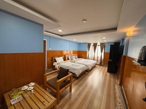 Hotellihuone, jossa on puulattia, sänky, jossa on kaksi tyynyä, puinen pöytä ja tuoli sekä televisio.