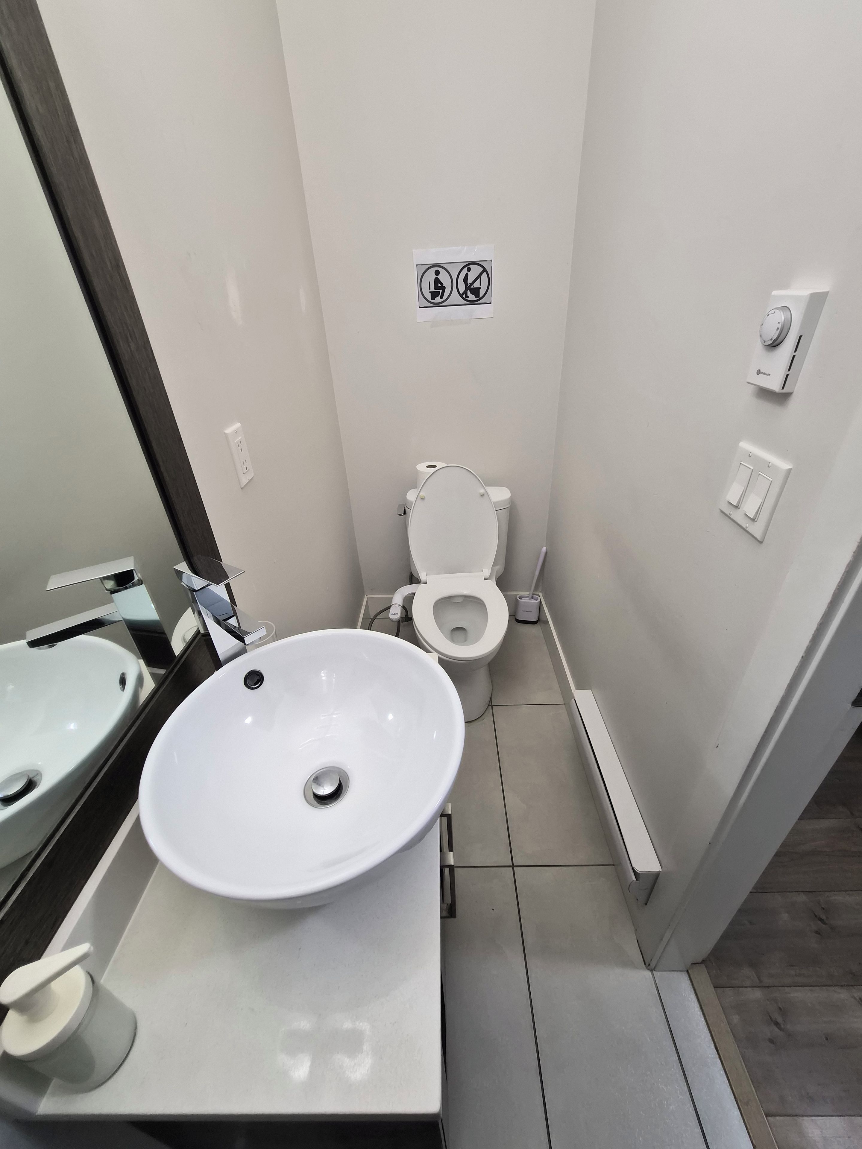 Une salle de bain avec un lavabo, des toilettes et un miroir, le tout de couleur blanche.