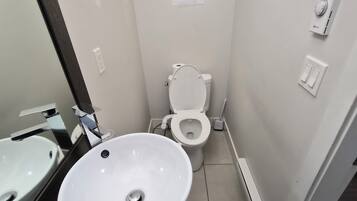 Une salle de bain avec un lavabo, des toilettes et un miroir, le tout de couleur blanche.