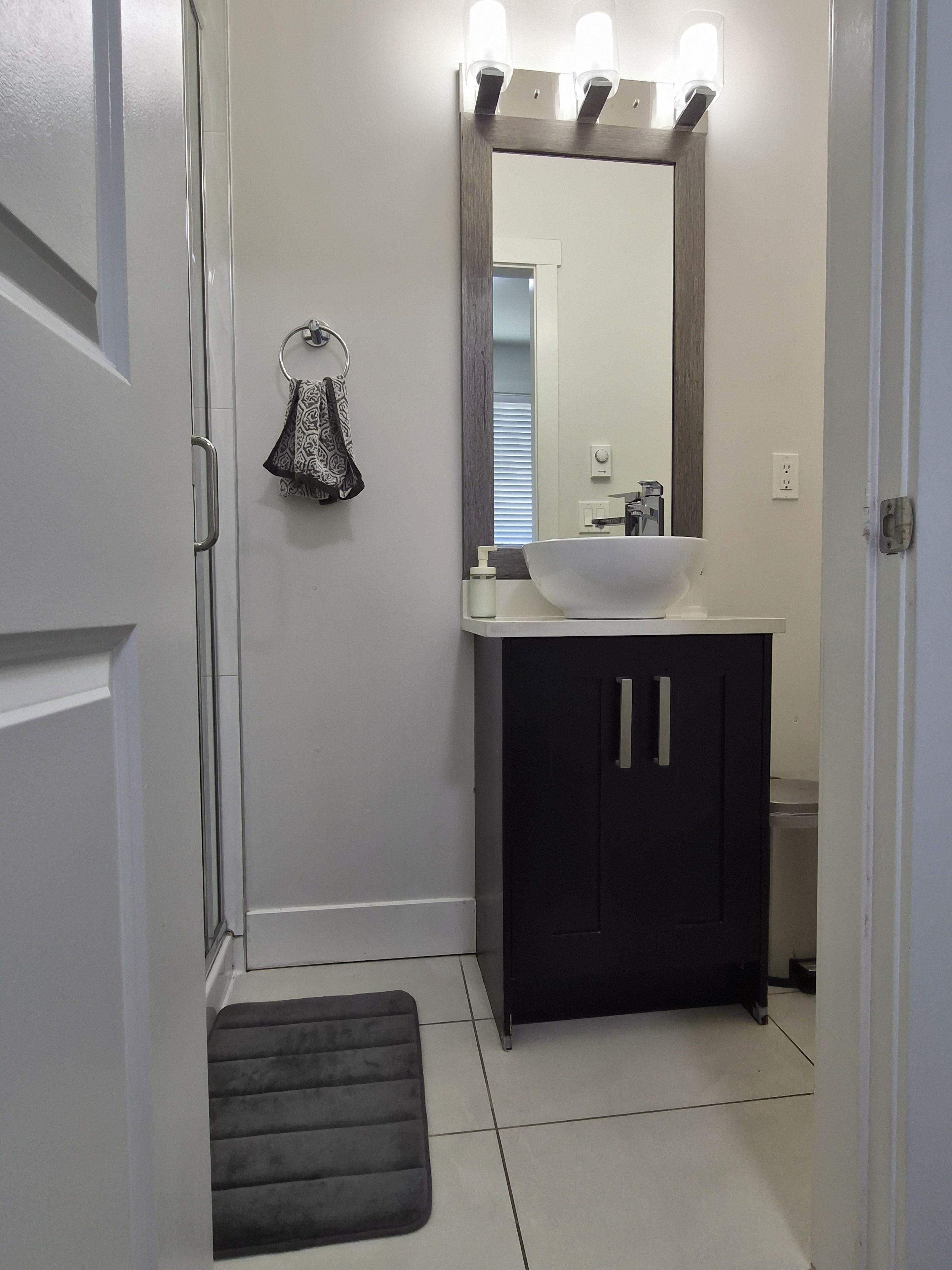A bathroom with a white sink, dark cabinets, a mirror with lights, and a towel rack.