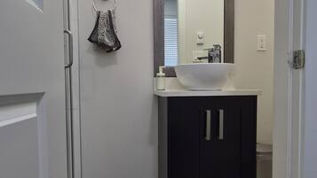 A bathroom with a white sink, dark cabinets, a mirror with lights, and a towel rack.