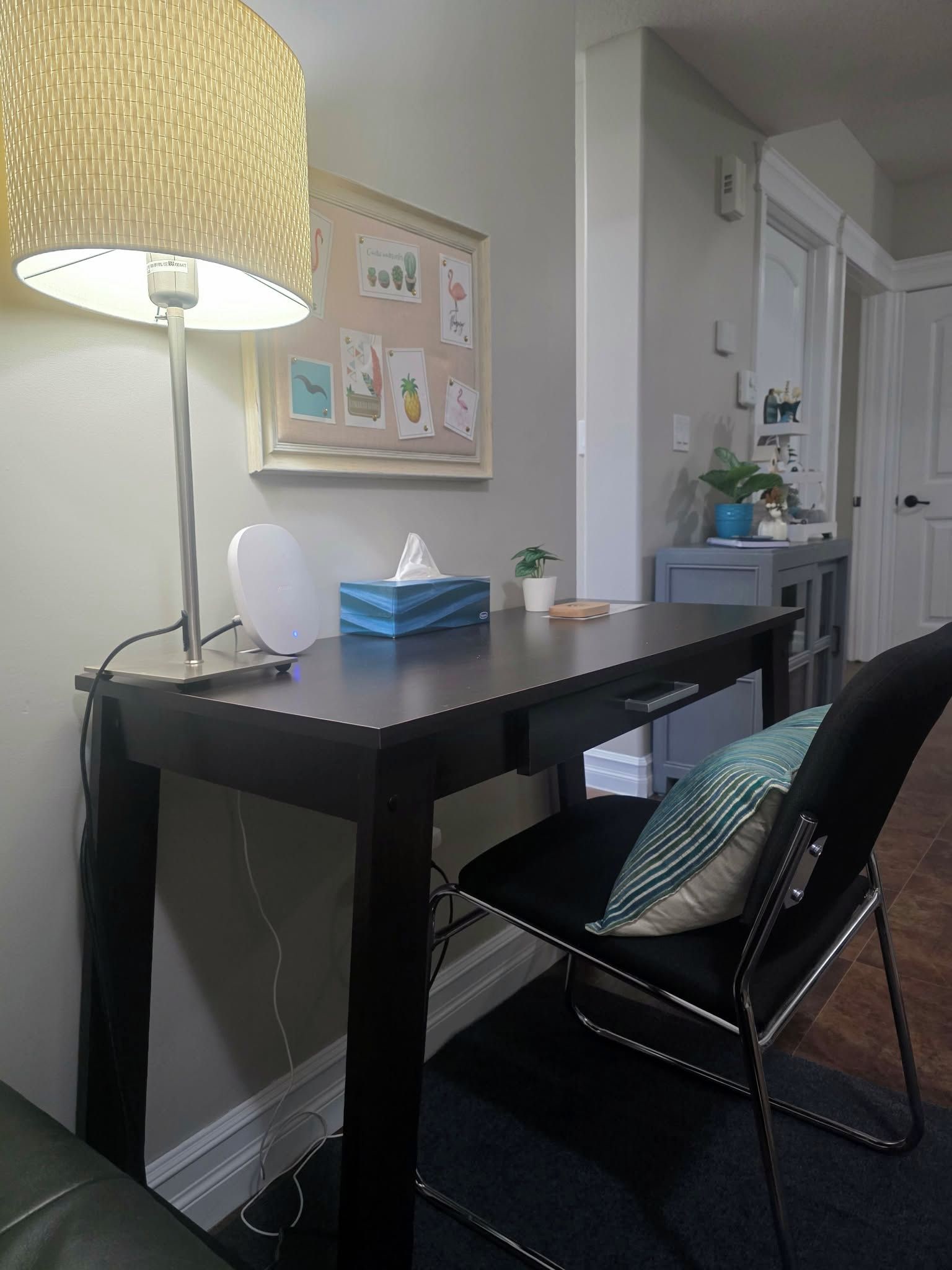 Une pièce comprenant un bureau, une chaise, une lampe et un mur orné de tableaux encadrés.