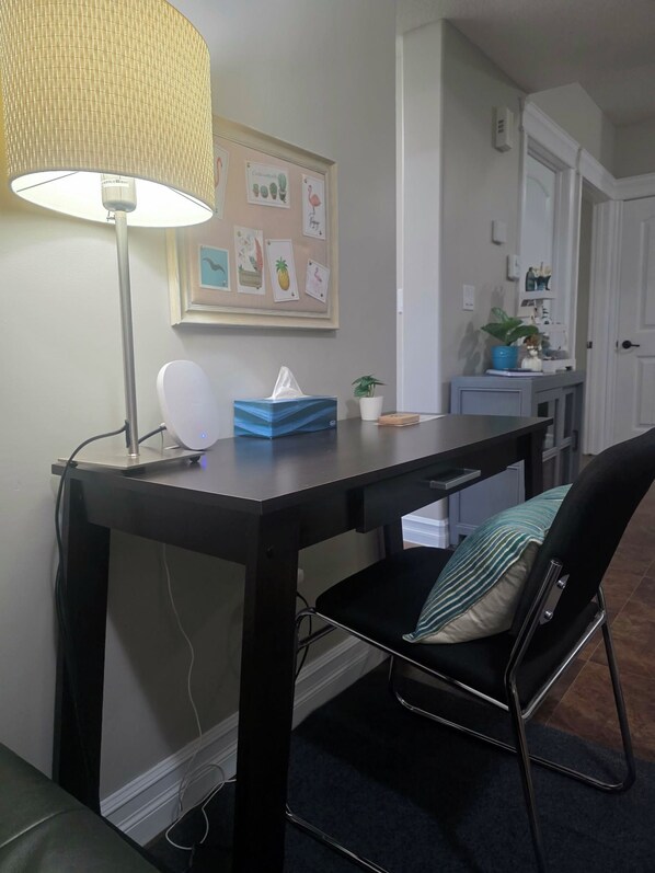 A room with a desk, chair, lamp, and a wall with framed pictures.