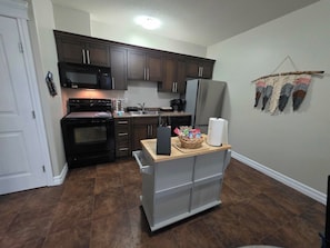 A compact kitchen with dark wooden cabinets, a black microwave, a stainless steel refrigerator, and a built-in oven. - The Bluebird Inn (Fort McMurray)