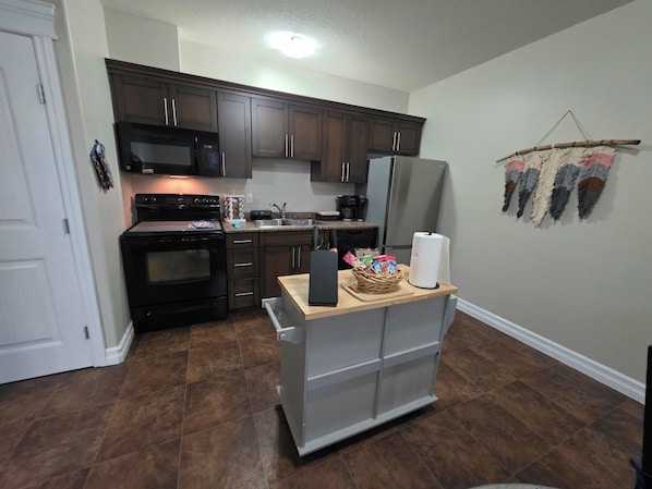 A compact kitchen with dark wooden cabinets, a black microwave, a stainless steel refrigerator, and a built-in oven.