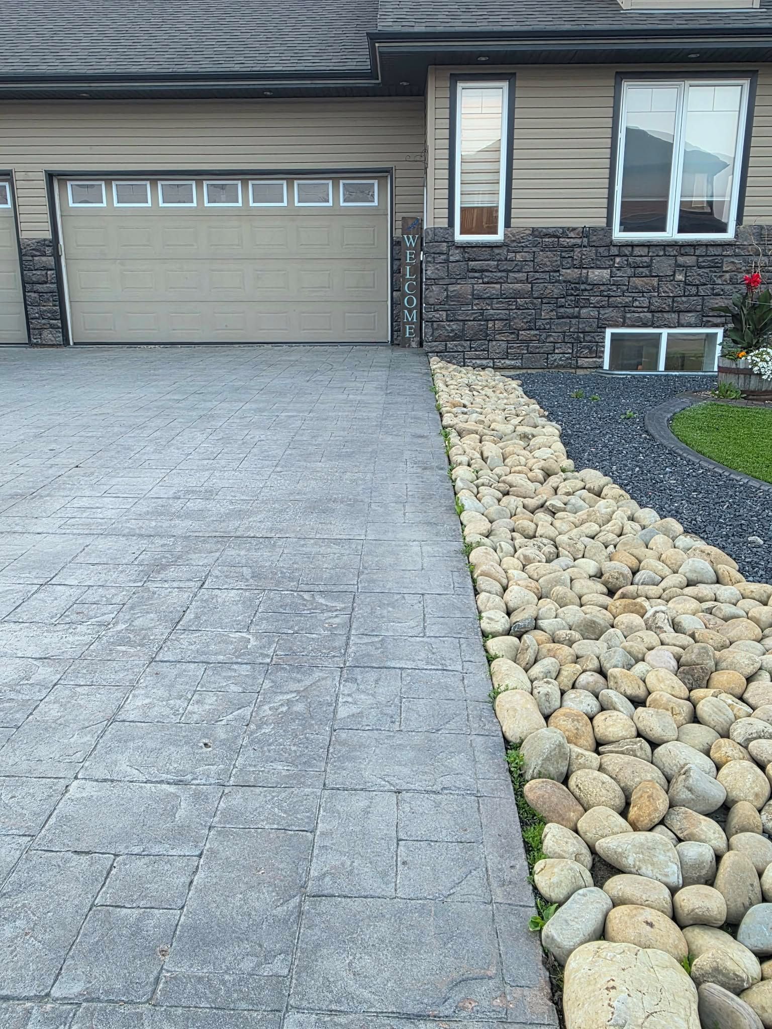 Une allée menant à une résidence, bordée de pierres, et une porte de garage.